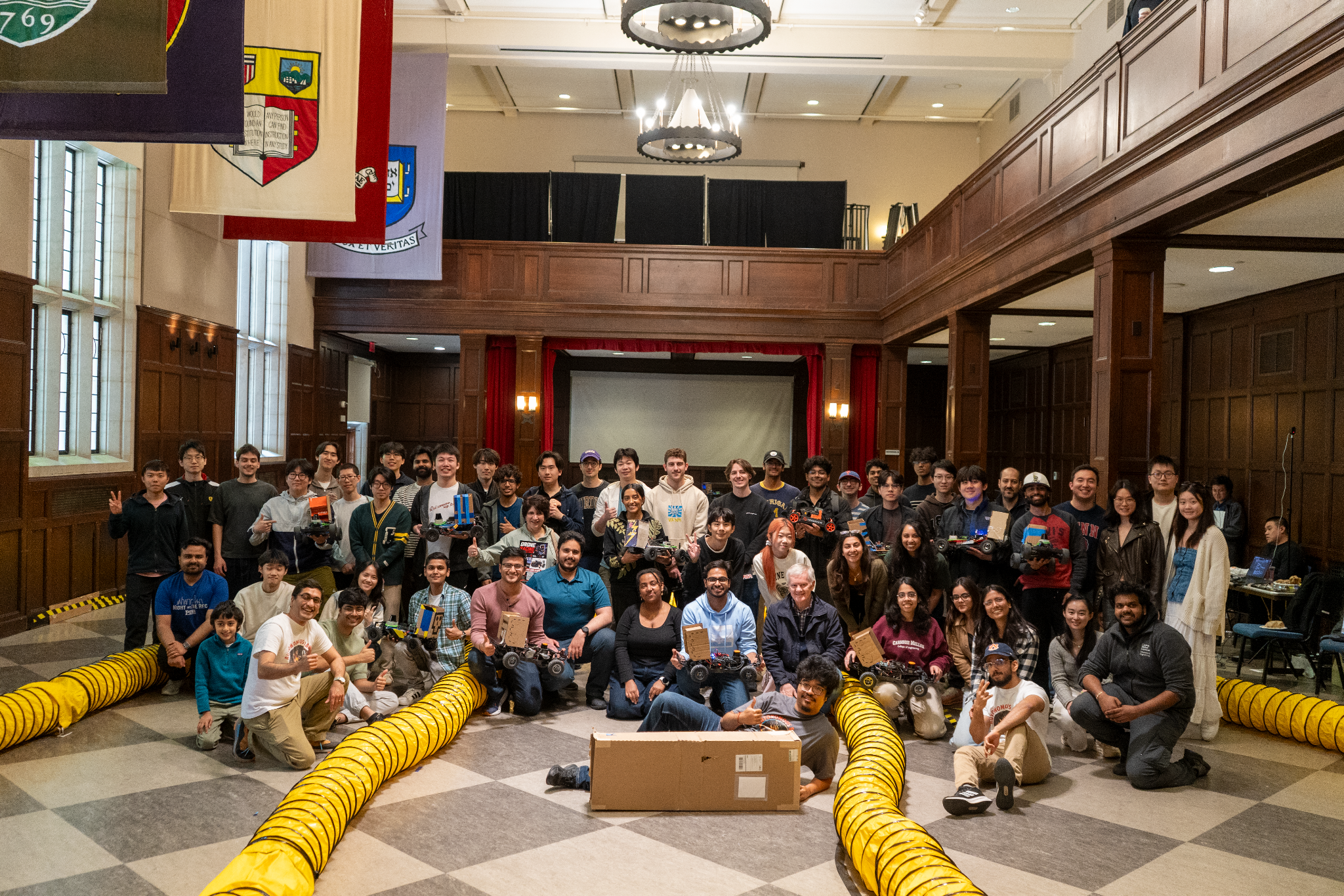 Autonomous racing students and instructors holding 1/10-scale cars beside a track with yellow barriers.